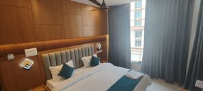 Hotelkamer met een groot bed, houten lambrisering, een plafondventilator en uitzicht op een gebouw.