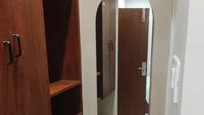 A bathroom with a wooden cabinet, a mirror, and a patterned rug. - Vaishnavi Inn (Rajahmundry)