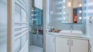 A modern bathroom with a glass shower enclosure, a white sink, and a mirror above it. - Invalides - The Collector (Paris)