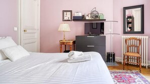 A bedroom with a bed, a dresser, a chair, a lamp, a radiator, and a mirror. - Invalides - The Collector (Paris)