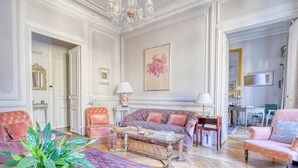 A spacious living room with a sofa set, a coffee table, and a chandelier. - Invalides - The Collector (Paris)