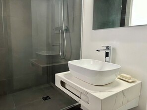 Een moderne badkamer met een wastafel, een douchecabine van glas en een spiegel boven de wastafel.