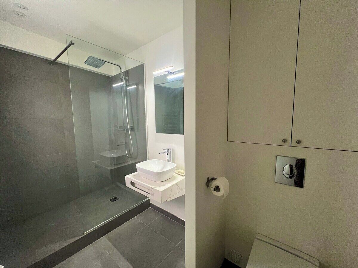 Een moderne badkamer met een douchecabine van glas, een witte wastafel en een toilet.