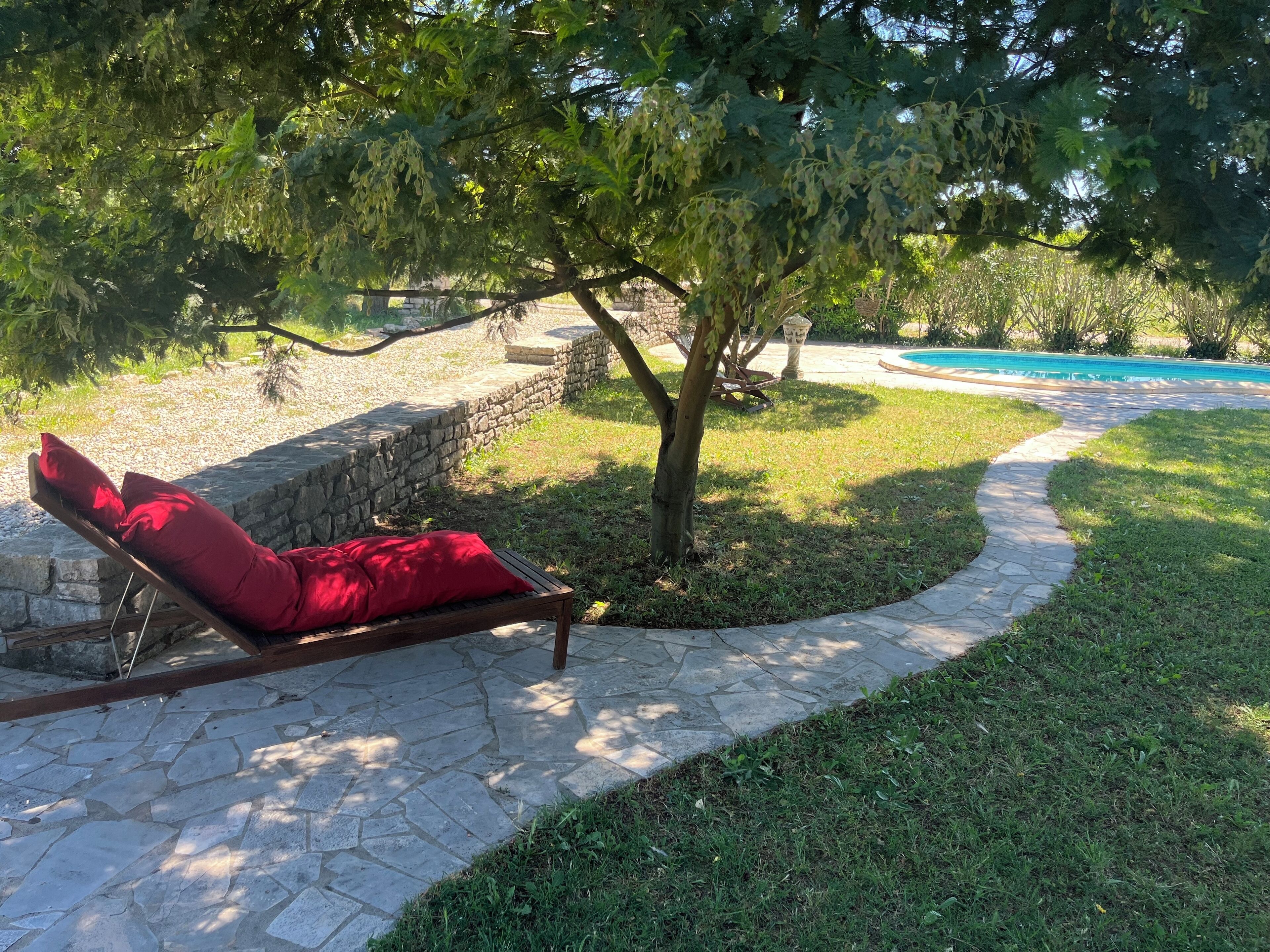 Un chemin de pierres mène à un fauteuil rouge placé sous un arbre.