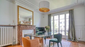 Un comedor con mesa de vidrio, dos sillas, chimenea y un ventanal con cortinas.