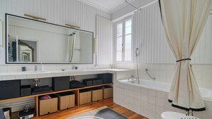 Un baño moderno con un espejo grande, dos lavamanos, una bañera y cestas de almacenamiento.