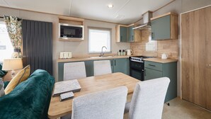 A compact kitchen with a microwave, stove, and sink. There is a dining table with chairs and a sofa. - Host & Stay | Grange (Morecambe)