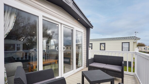 A covered outdoor patio with wicker furniture and sliding glass doors leading to a deck. - Host & Stay | Grange (Morecambe)