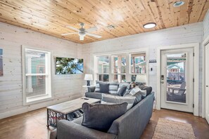 A cozy living room with a wooden ceiling, a ceiling fan, and a large window with blinds. - Beautiful 3 Bdr | Community Pool | Pets | Sleeps 10 (Port Aransas)