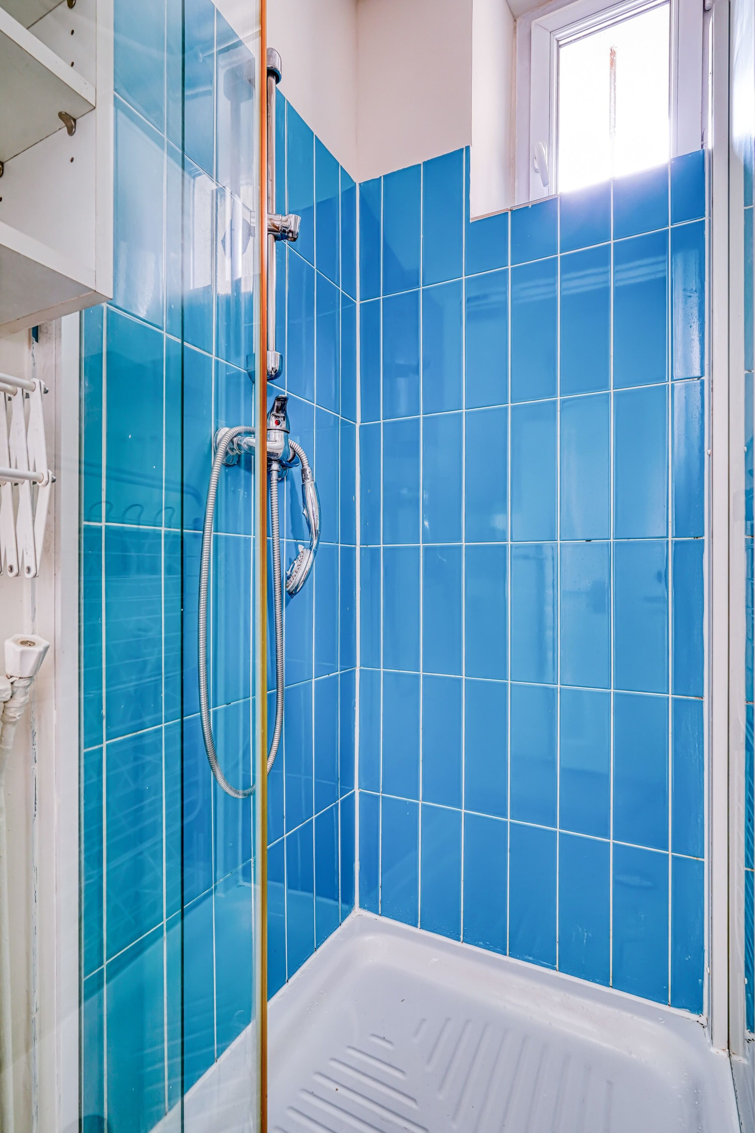 Un baño con paredes de azulejos azules, una bañera blanca y un cabezal de ducha.
