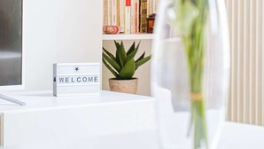A white table with a clear vase containing pink and white flowers, a small potted plant, and a welcome sign. - Ternes district - The Dreamer (Paris)
