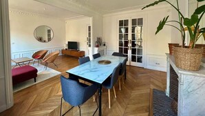 Ein geräumiges Zimmer mit großem Esstisch, bequemen Sitzgelegenheiten, einem Kamin und einem großen Fenster.