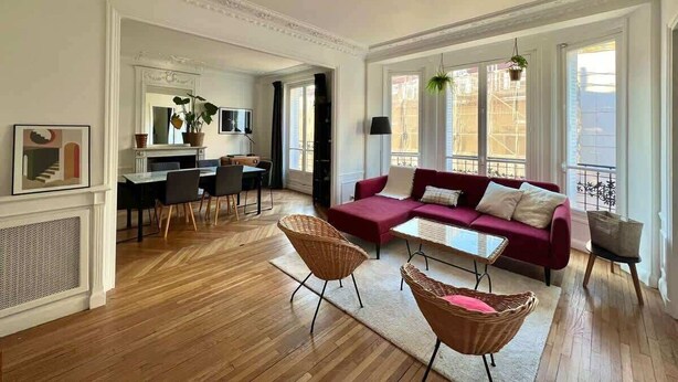 Ein geräumiges Wohnzimmer mit einem roten Sofa, einem Essbereich mit Tisch und Stühlen sowie großen Fenstern mit Blick auf die Stadt.