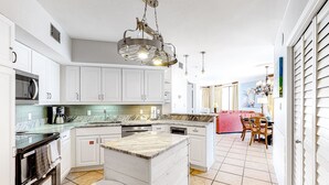A modern kitchen with white cabinetry, a central island, and a dining area with a red sofa.