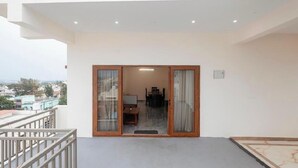 A balcony with a view of the city, a dining area with a table and chairs, and a sliding glass door leading to an interior space. - Aetheria Service Apartments (Chikkamagaluru)