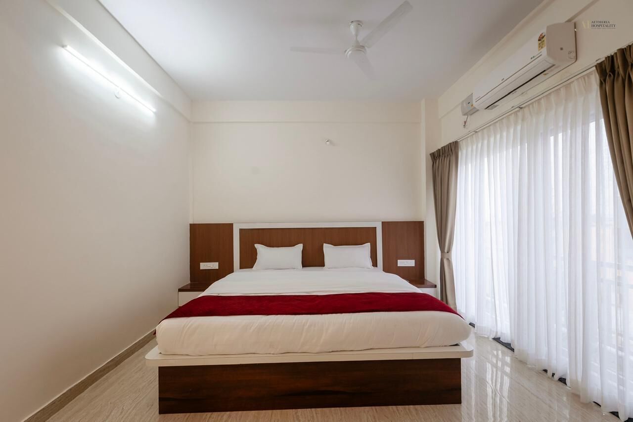 A hotel room with a bed, ceiling fan, air conditioning unit, and a window with curtains.