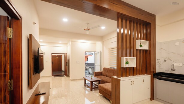 A modern living room with a sofa, a coffee table, a TV, and a kitchen area with cabinets and a countertop. - Aetheria Service Apartments (Chikkamagaluru)