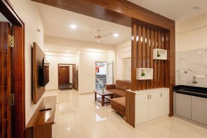 Una sala de estar moderna con sofá, mesa de centro, televisor y una zona de cocina con armarios y encimera.