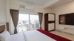 A hotel room with a bed, a TV, a wardrobe, and a balcony with a city view. - Aetheria Service Apartments (Chikkamagaluru)