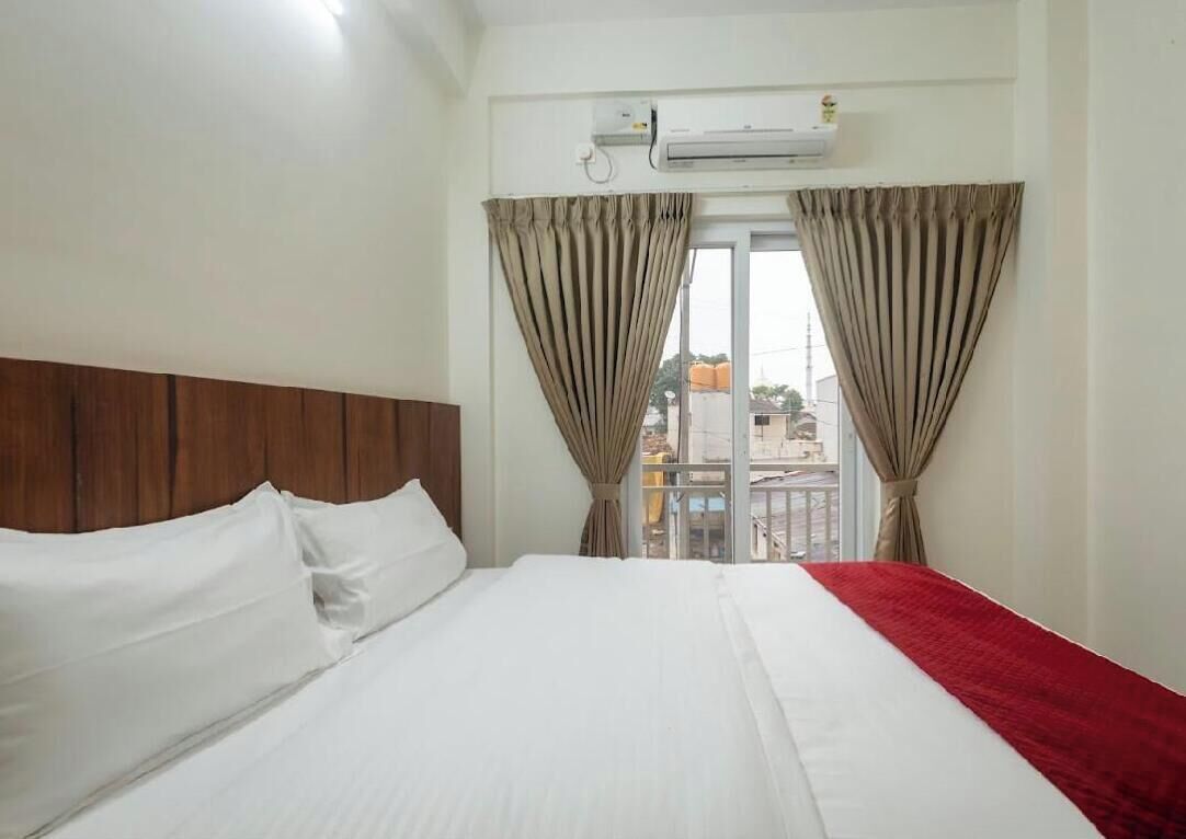 A hotel room with a bed, curtains, an air conditioning unit, and a view of the outside.