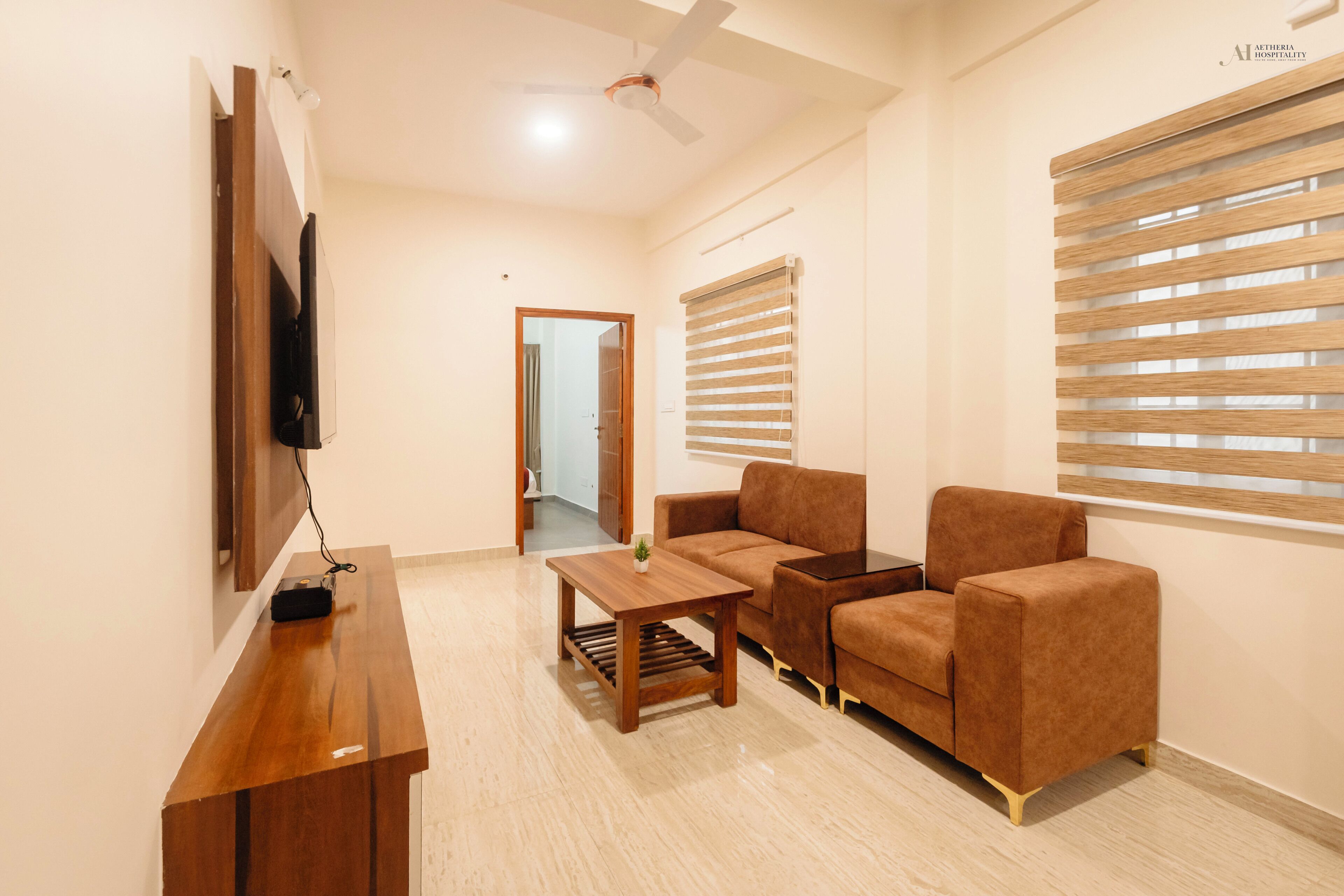 A modern living room with a flat-screen TV, wooden coffee table, brown sofa, and a ceiling fan.