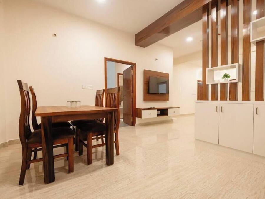 A dining area with a wooden table and chairs, a TV mounted on the wall, and a cabinet with shelves.