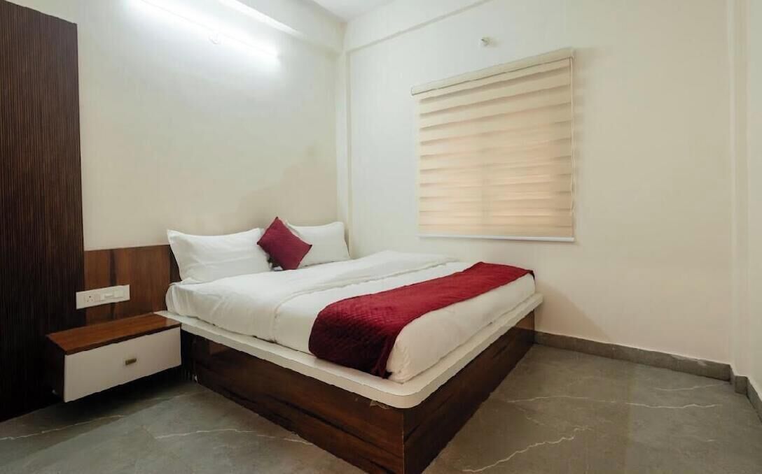 Een slaapkamer met een bed, nachtkastje, houten hoofdbord, raam met zonwering en een stopcontact.