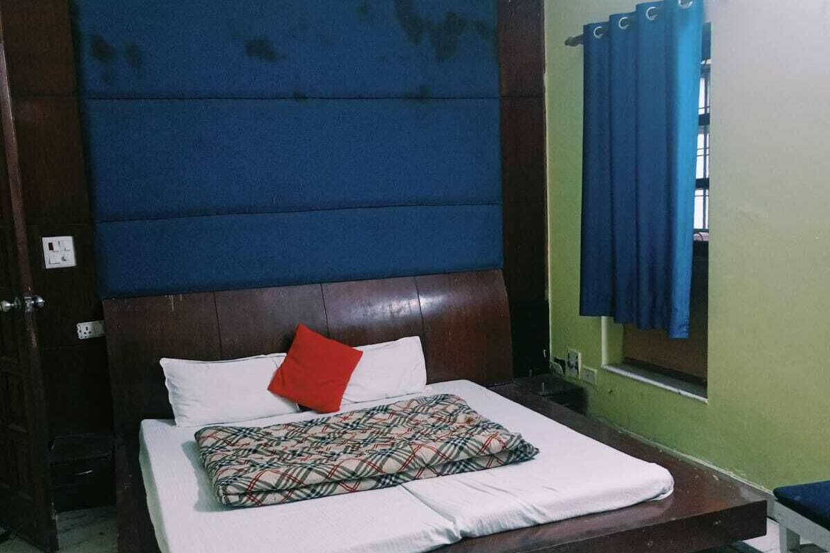 A bedroom with a large bed, a wooden headboard, a window with blue curtains, and a green wall.