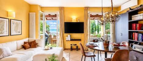 Una sala de estar moderna con un sofá, una zona de comedor con mesa y sillas, un televisor montado en la pared y una estantería.