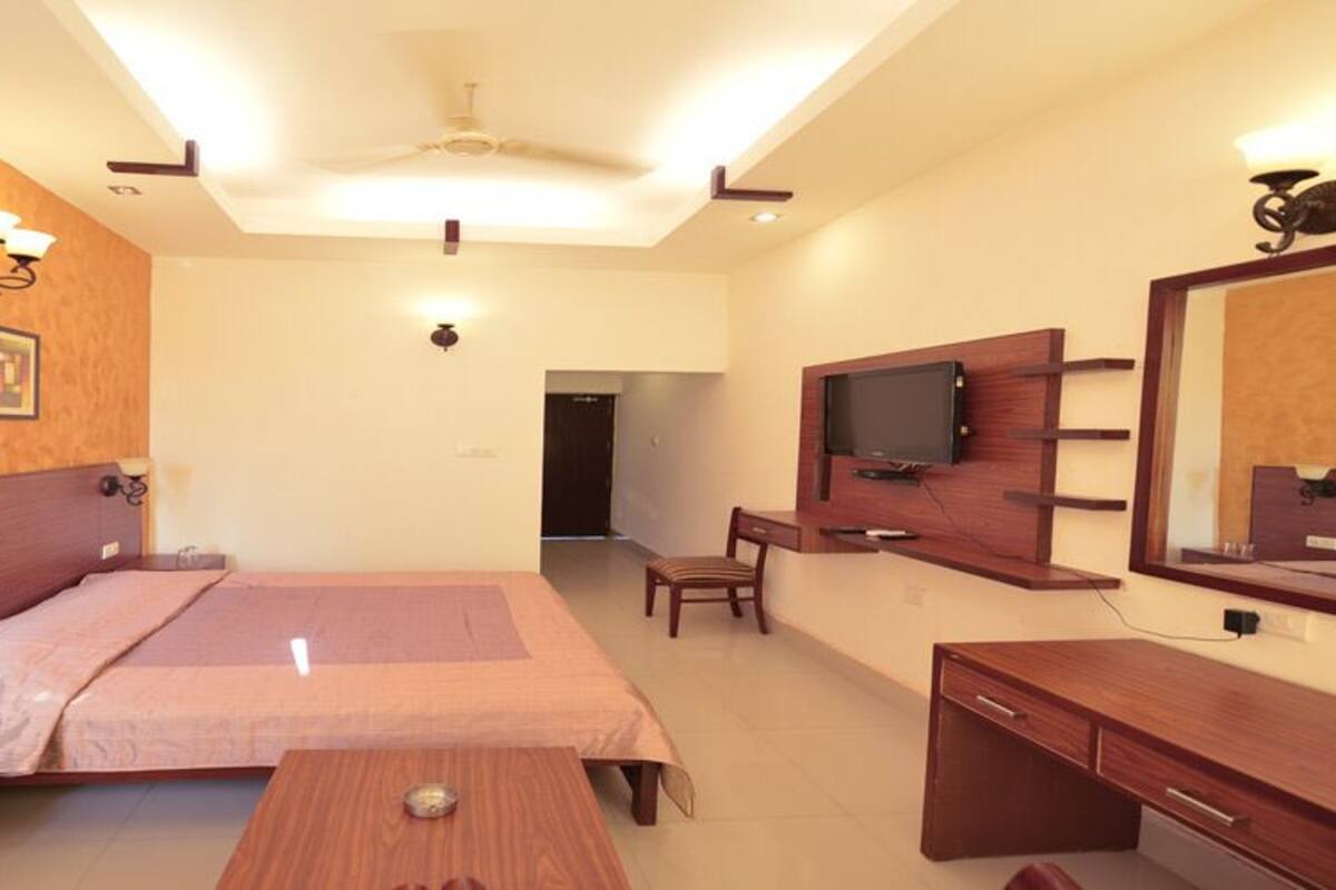 A hotel room with a bed, bedside tables, a desk, a chair, a TV, and a mirror.