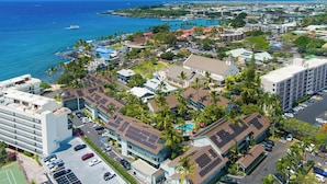 An aerial view of a coastal city with a marina, buildings with solar panels, and a clear view of the ocean.