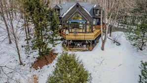 A cabin with a wooden deck, large windows, and a covered outdoor seating area. - Whitman Brook Overlook House with Game Room (Quechee)