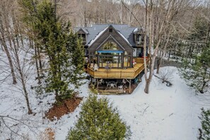 A cabin with a wooden deck, large windows, and a covered outdoor seating area. - Game Room - Whitman Brook Overlook (Quechee)