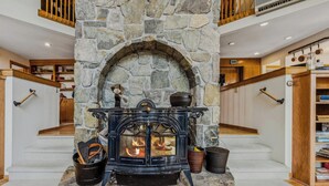 A stone fireplace with a black wood-burning stove, a stone arch, and a wooden staircase. - Whitman Brook Overlook House with Game Room (Quechee)