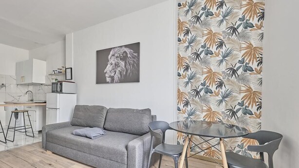 Un salon moderne avec un canapé gris, une table basse en verre et un papier peint à motifs.