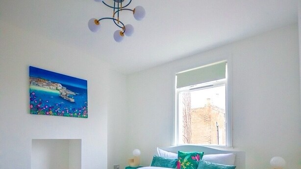 Un dormitorio con cama, ventana, un cuadro y una lámpara en el techo.