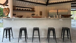 A covered outdoor bar area with a concrete countertop, black stools, and various barware. - Kooteja Aurora Coronado Nature with Private Pool (Las Lajas)