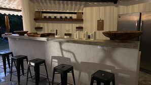 An outdoor bar area with a concrete countertop, wooden stools, and a stainless steel refrigerator. - Kooteja Aurora Coronado Nature with Private Pool (Las Lajas)