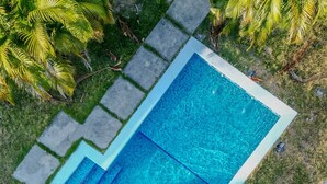 An aerial view of a rectangular swimming pool with clear blue water, surrounded by stone tiles and grass. - Kooteja Aurora Coronado Nature with Private Pool (Las Lajas)