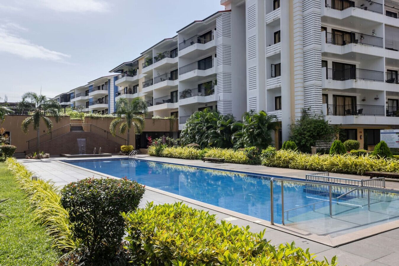 A modern hotel with a swimming pool surrounded by lush greenery and a multi-story building with balconies.