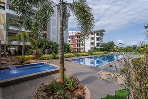 A hotel pool area with a palm tree, a small waterfall feature, and a clear sky.
