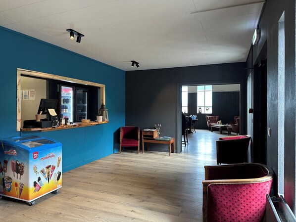 A modern interior with a blue wall, a counter with a beverage dispenser, and seating areas.