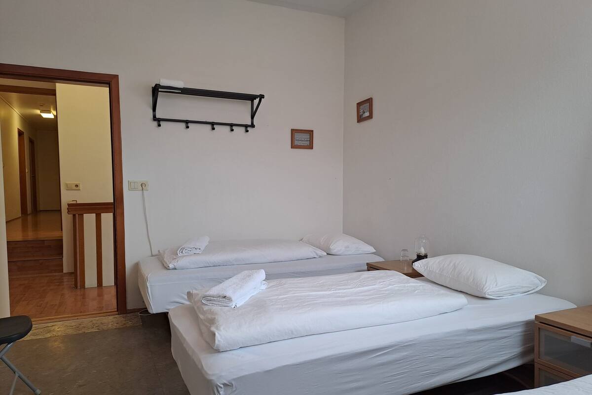 A hotel room with two single beds, a wooden nightstand, a small table, and a wall-mounted shelf.