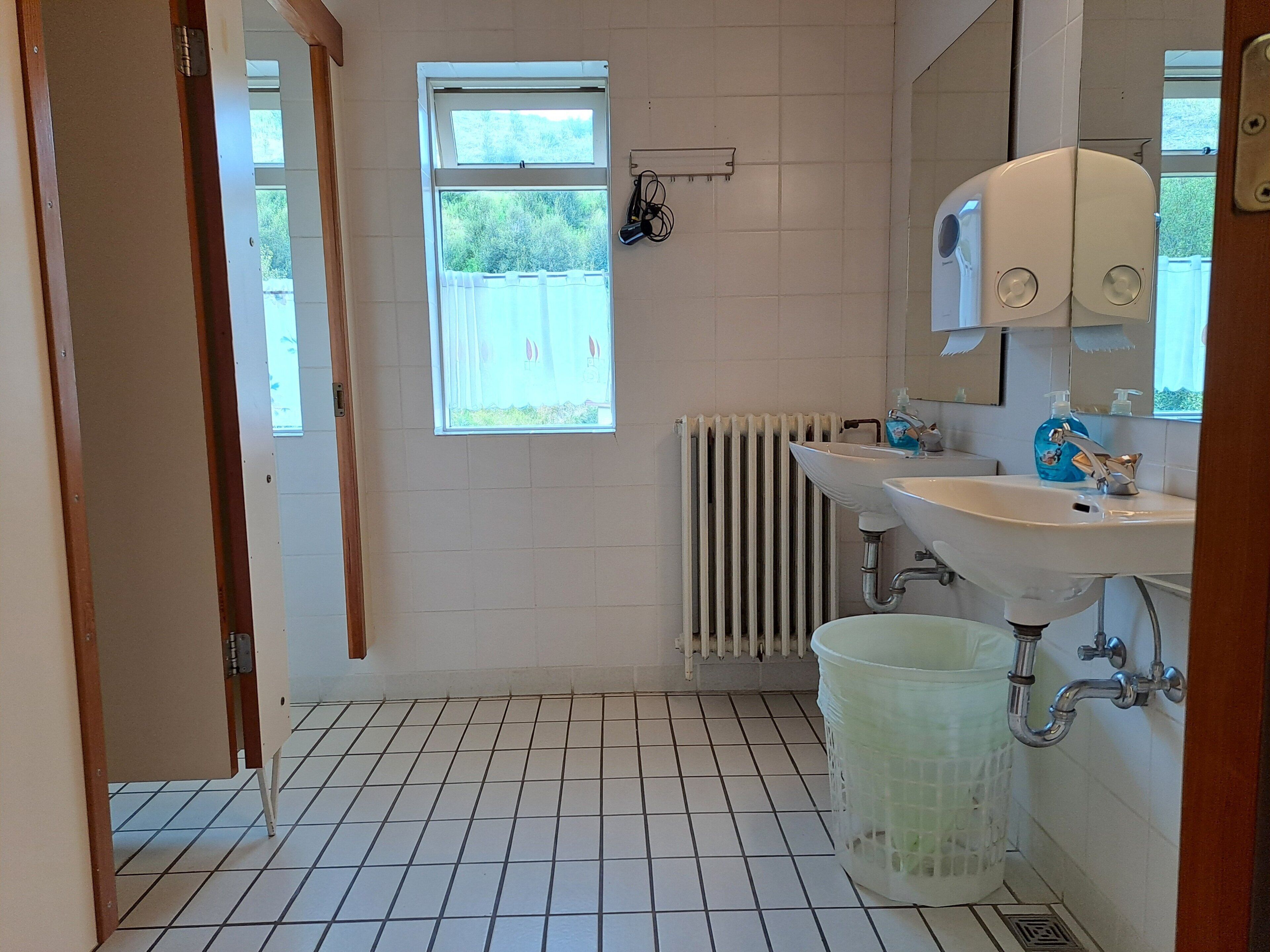 Une salle de bain avec deux lavabos, une fenêtre, un radiateur et une poubelle.