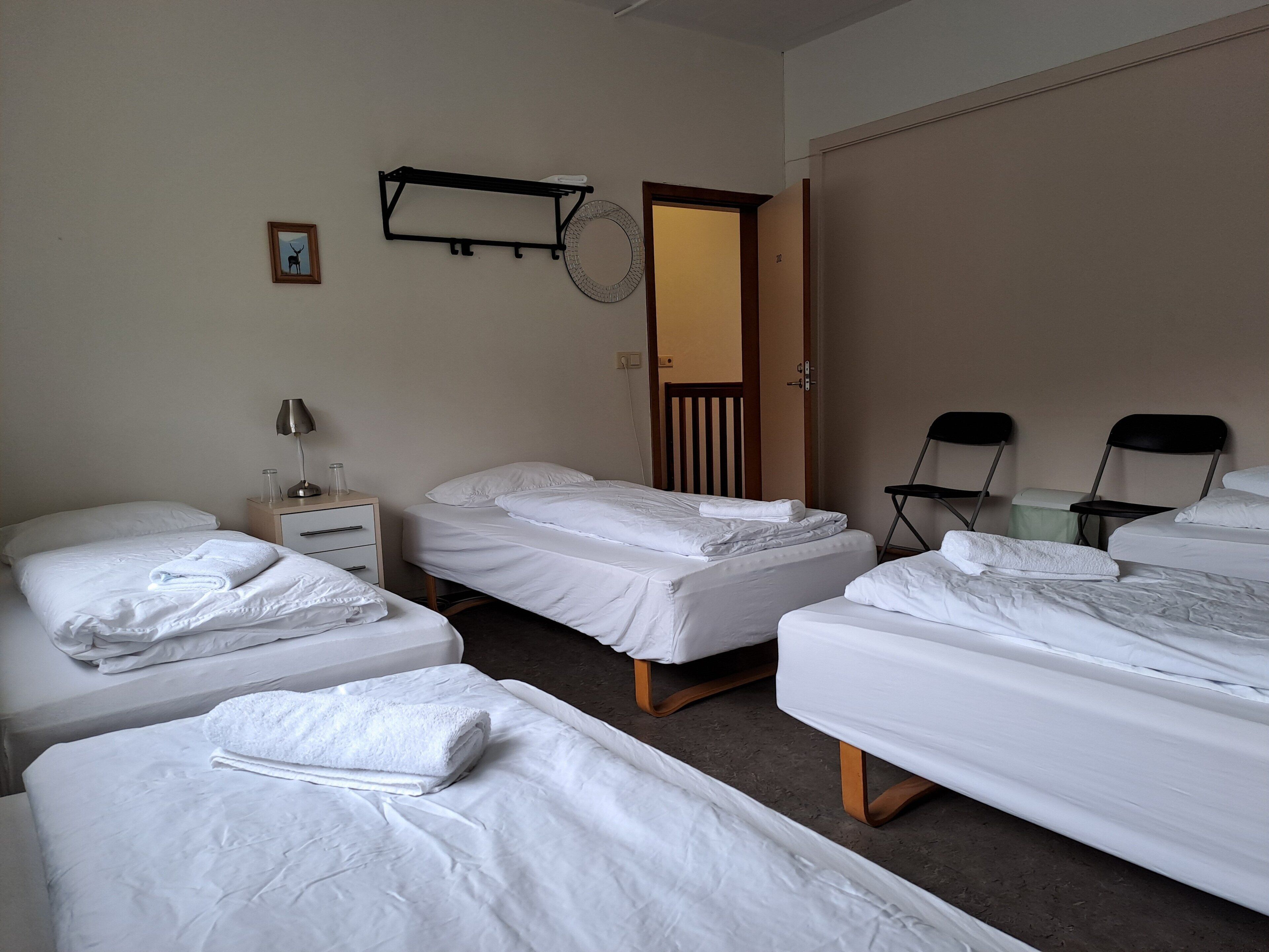 A hotel room with four single beds, a bedside table with a lamp, a small picture frame, and a door leading to a bathroom.