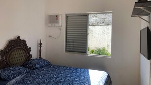 Et soveværelse med seng, et vindue med rullegardiner, en fastgjort aircondition og et fjernsyn på væggen.