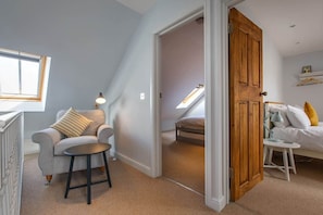 A room with a loft bed, a small table with a lamp, a sofa with a cushion, and a radiator.