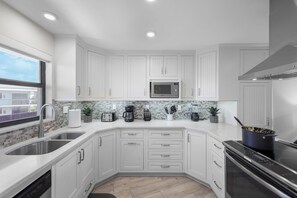 A modern kitchen with white cabinetry, a stainless steel sink, a microwave, a stove, and a dishwasher.
