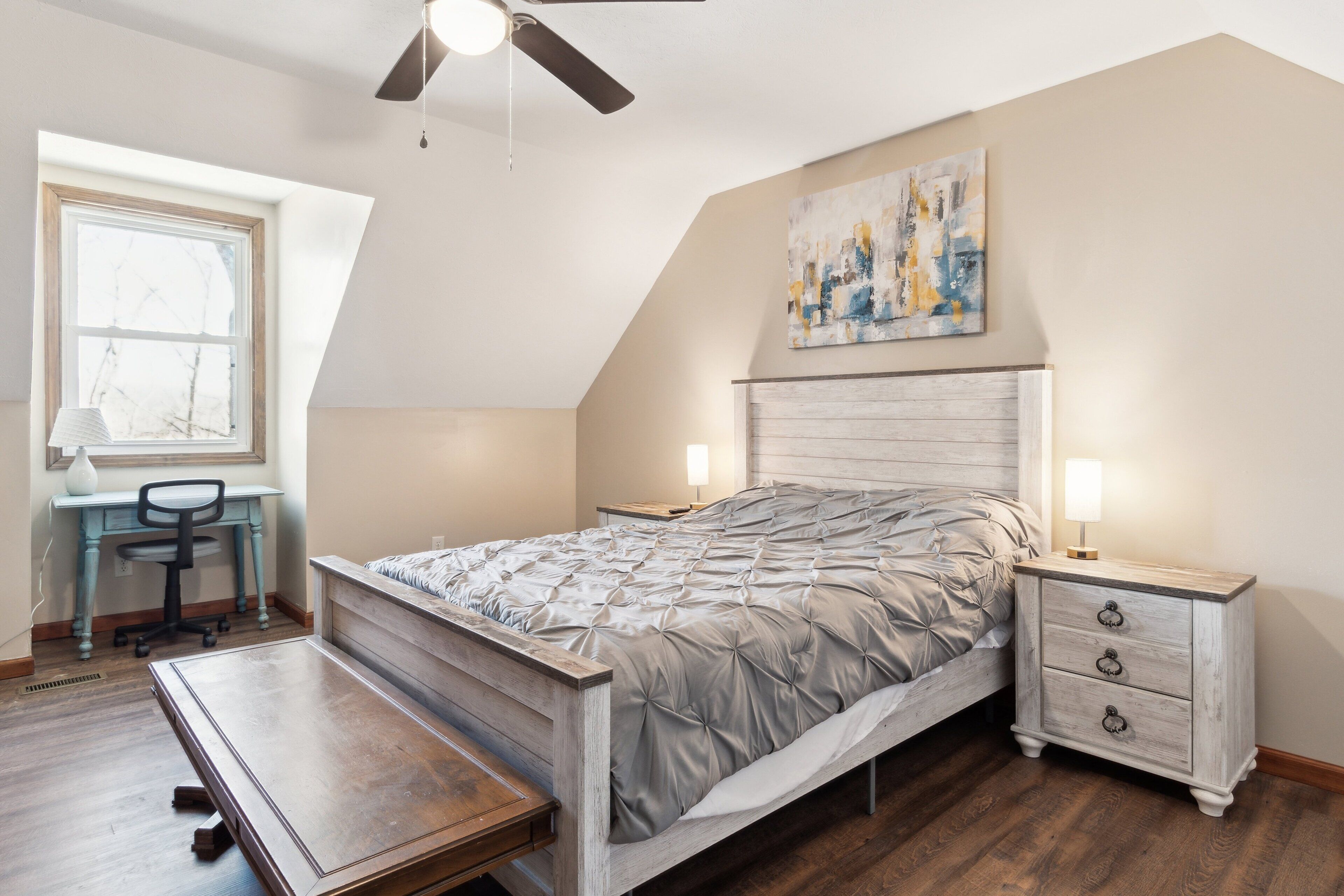 A bedroom with a bed, desk, chair, and nightstands.