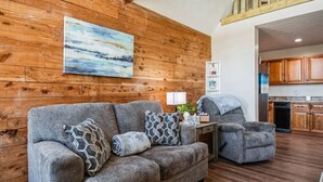 A living room with a wooden wall, a gray sofa, a gray armchair, and a painting.